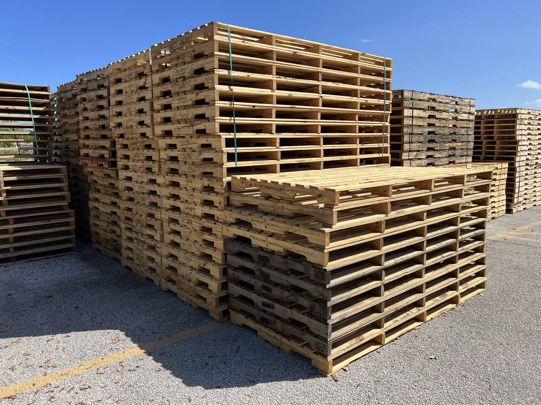 Bulk new wood pallets stacked in Florida pallet supplier yard sunny day